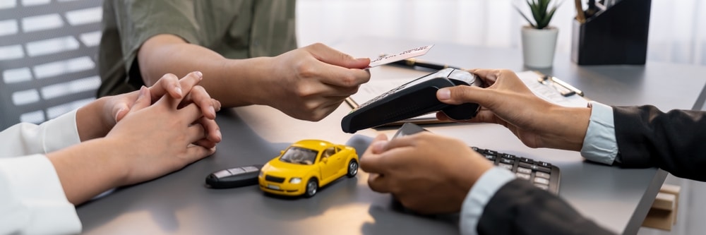 People exchanging car keys across a desk beside a yellow toy car