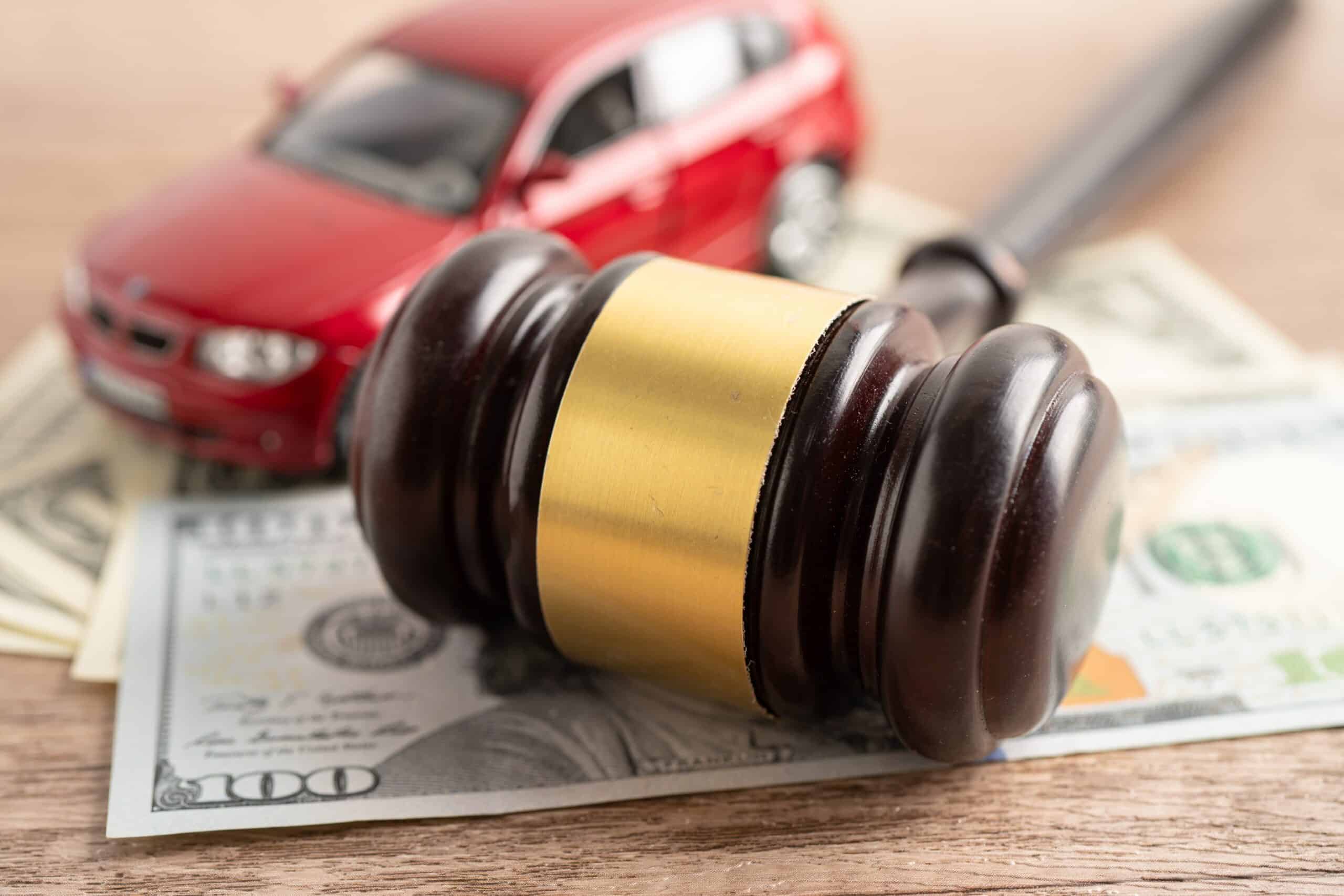 Wooden judge's gavel resting on cash beside a red toy car