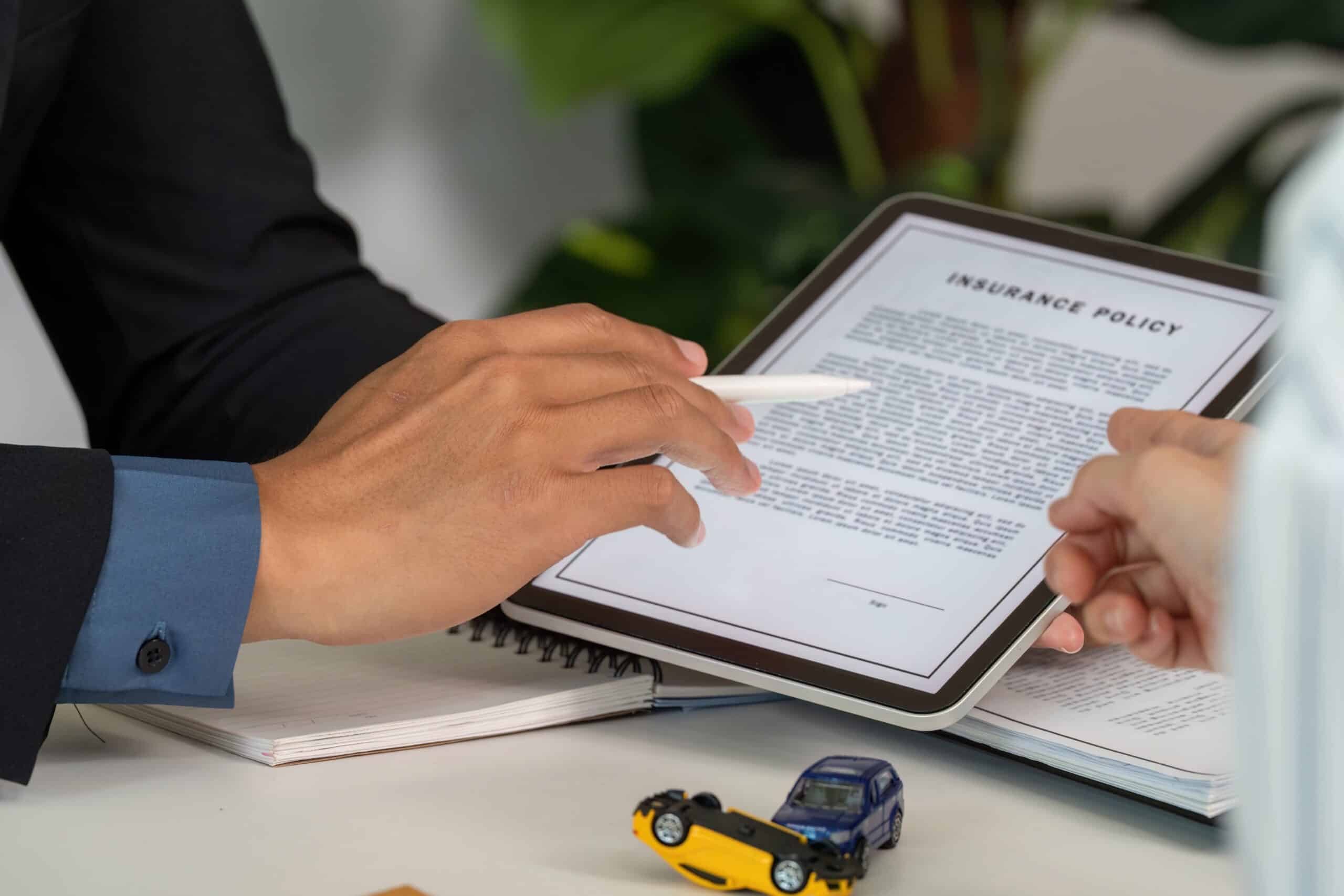 Hands pointing to details on an auto insurance policy document beside a toy car