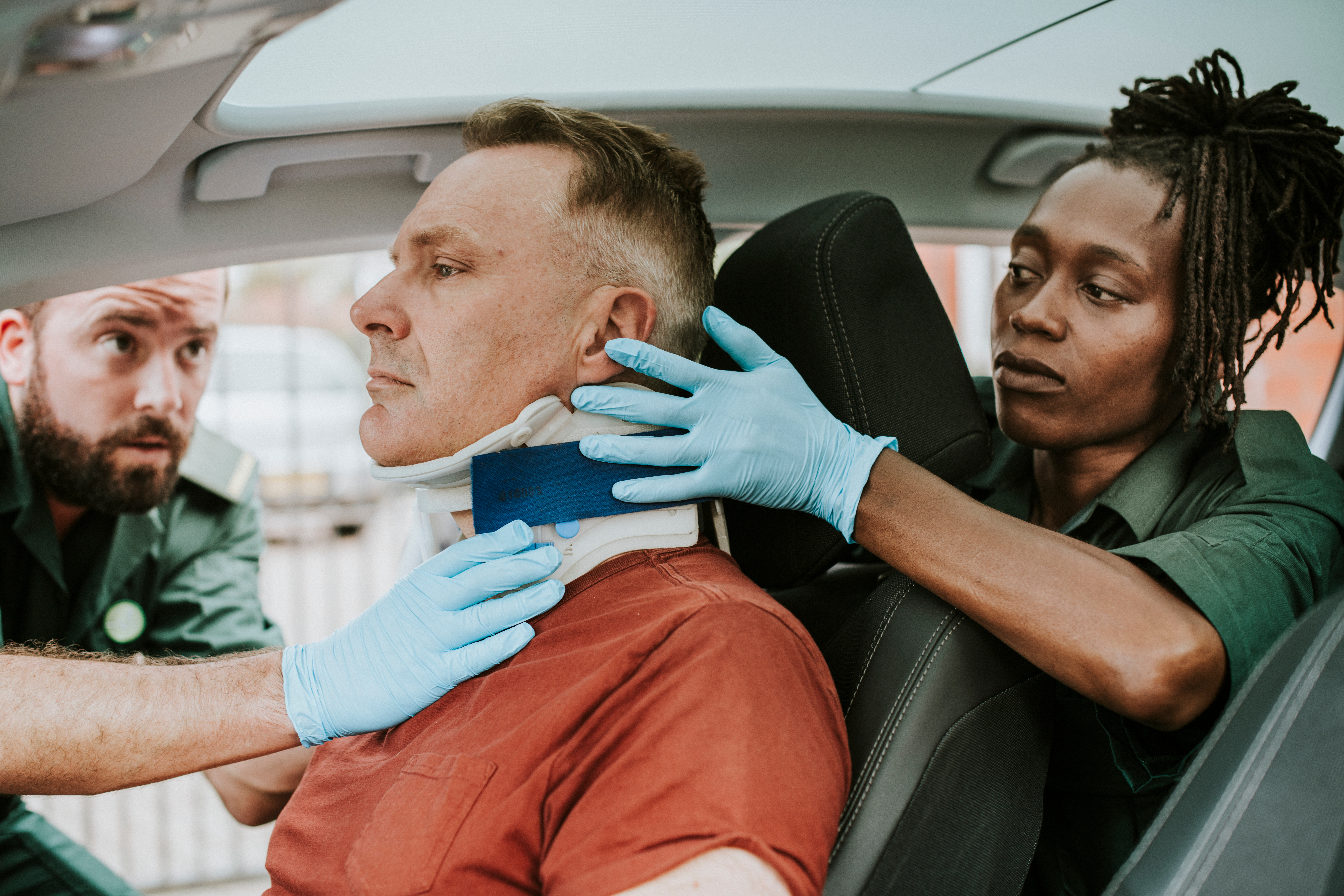 Paramedics fitting a neck brace on an injured man inside a vehicle
