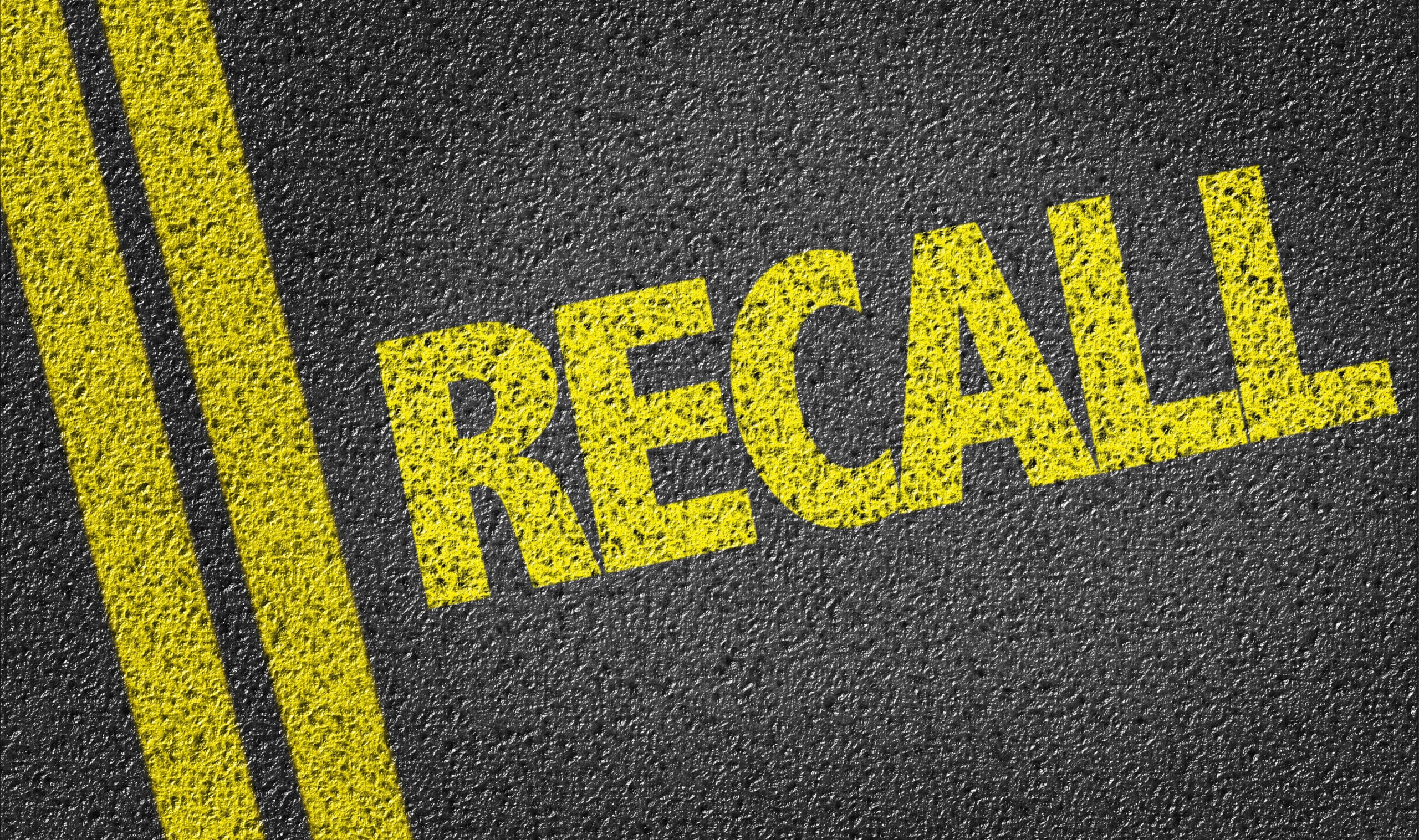 The word Recall painted in yellow across an asphalt road