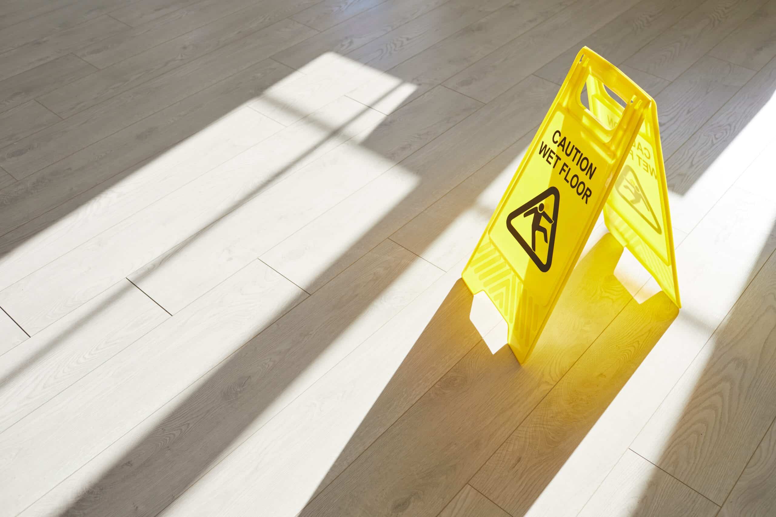 Yellow wet floor caution sign on a hardwood floor in sunlight