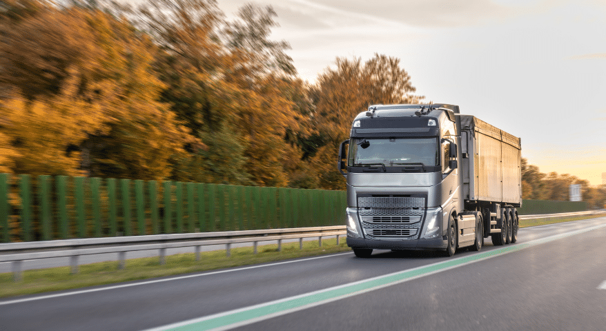 White semi truck driving on a highway lined with autumn trees