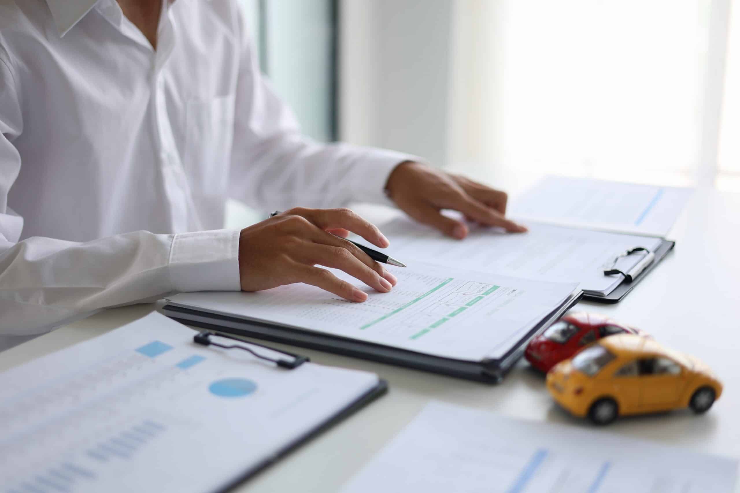 Hands reviewing an insurance document on a clipboard beside a toy car