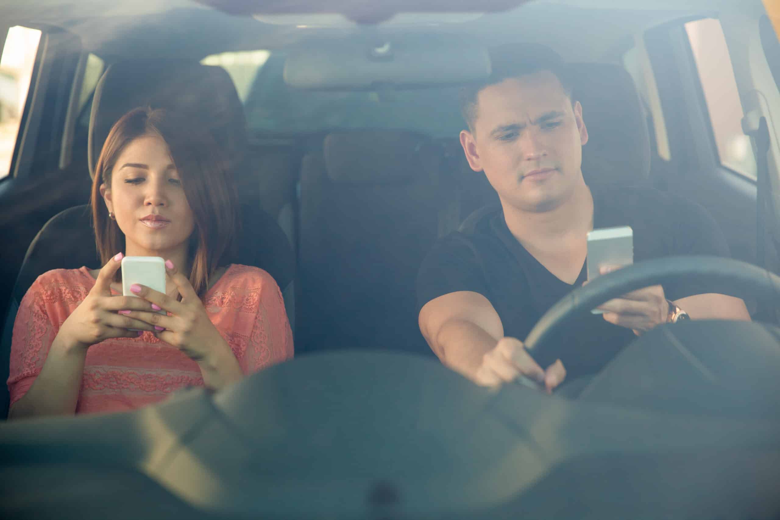 Passenger looking at her phone while a man drives the car