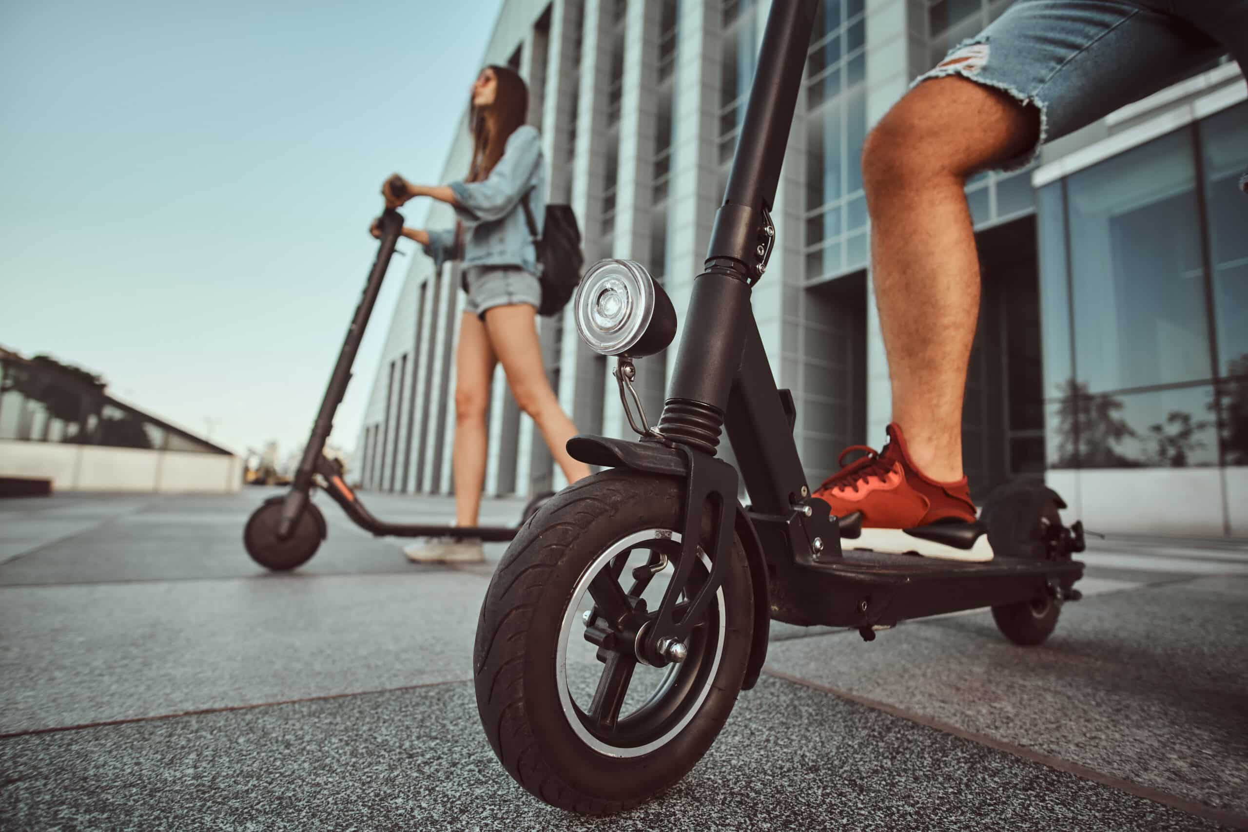 People riding electric scooters along a city sidewalk