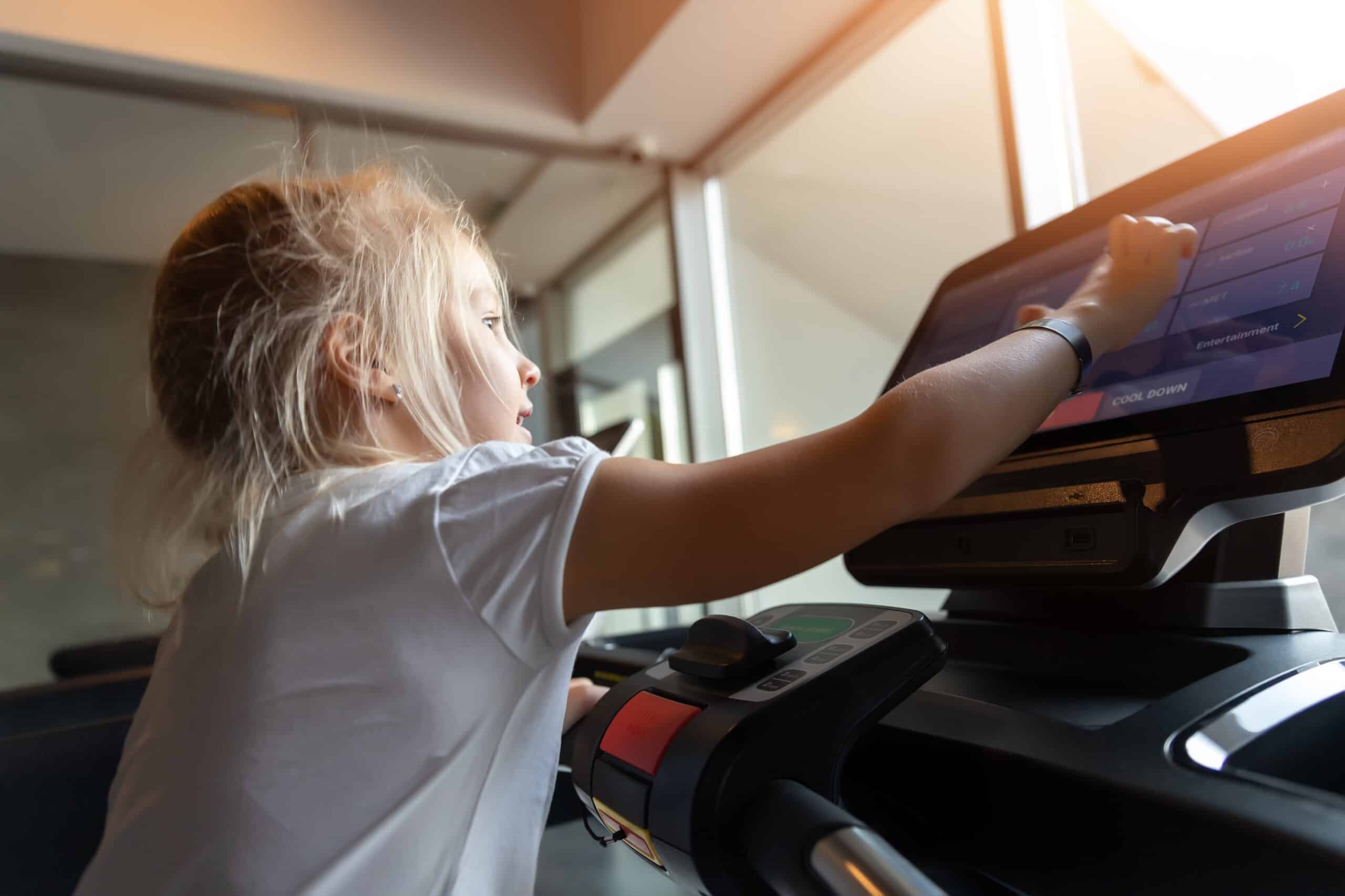 Young child reaching up to the console of a treadmill at home