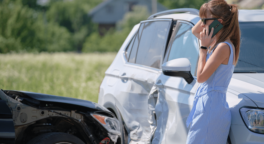 Woman on her phone beside a damaged car after a collision