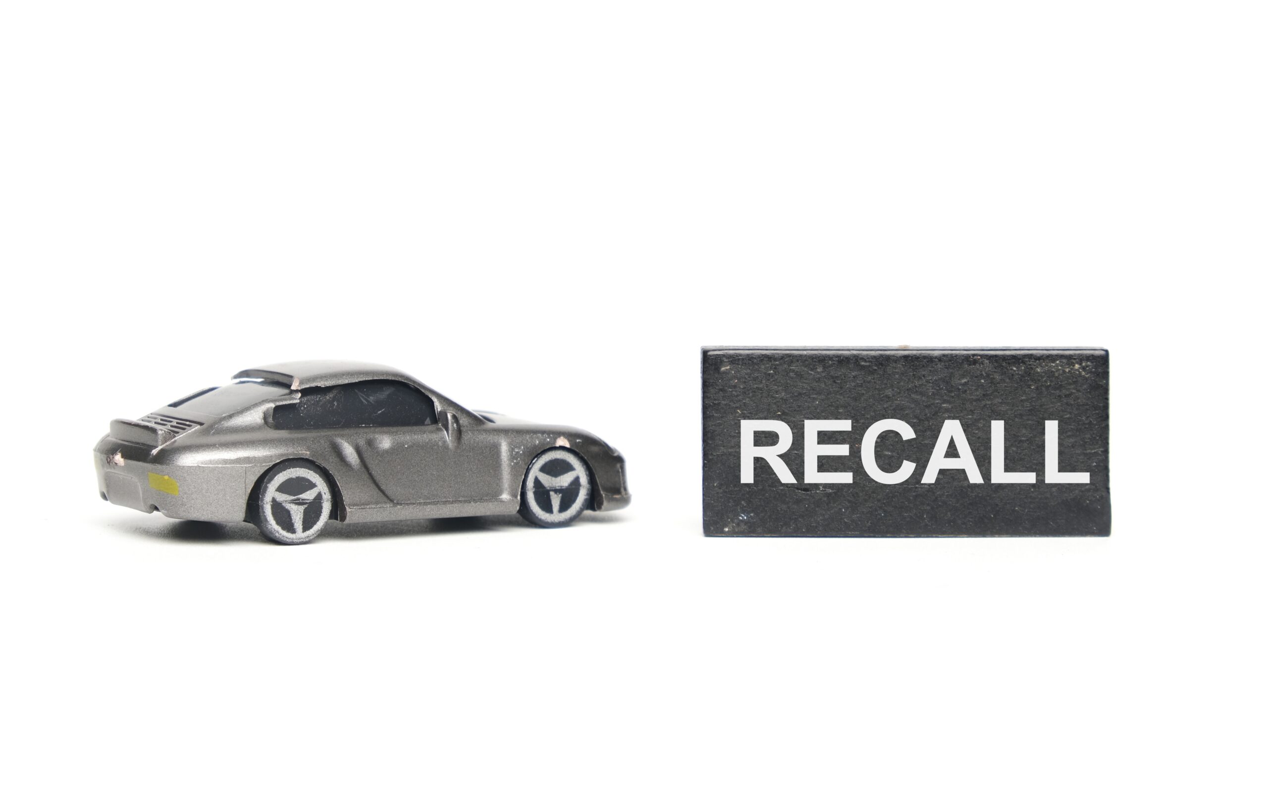 Gray toy sports car beside a Recall sign