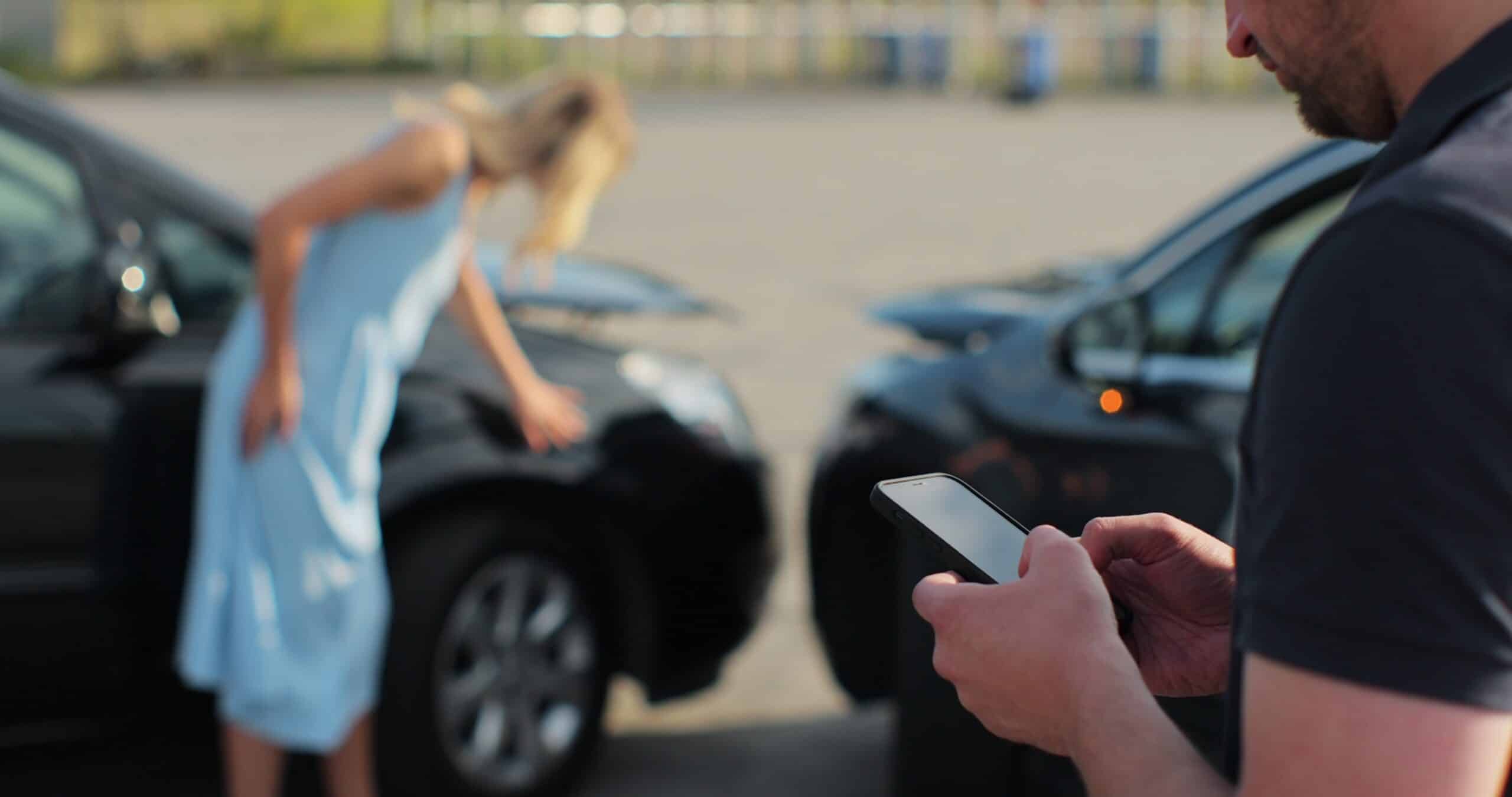 Woman inspecting damage on a black car after a collision while a man uses his phone