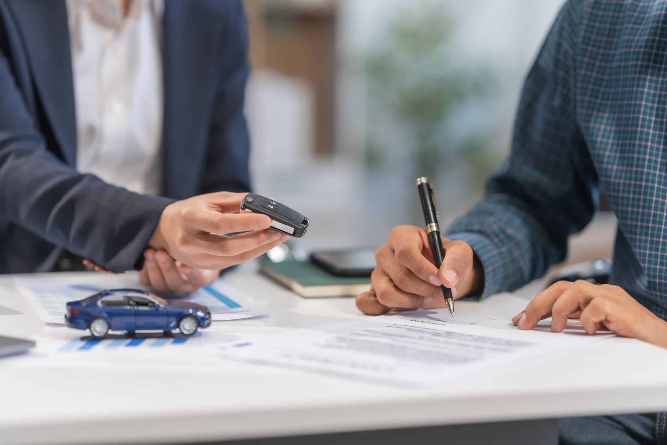 Hand passing car keys over paperwork on a desk