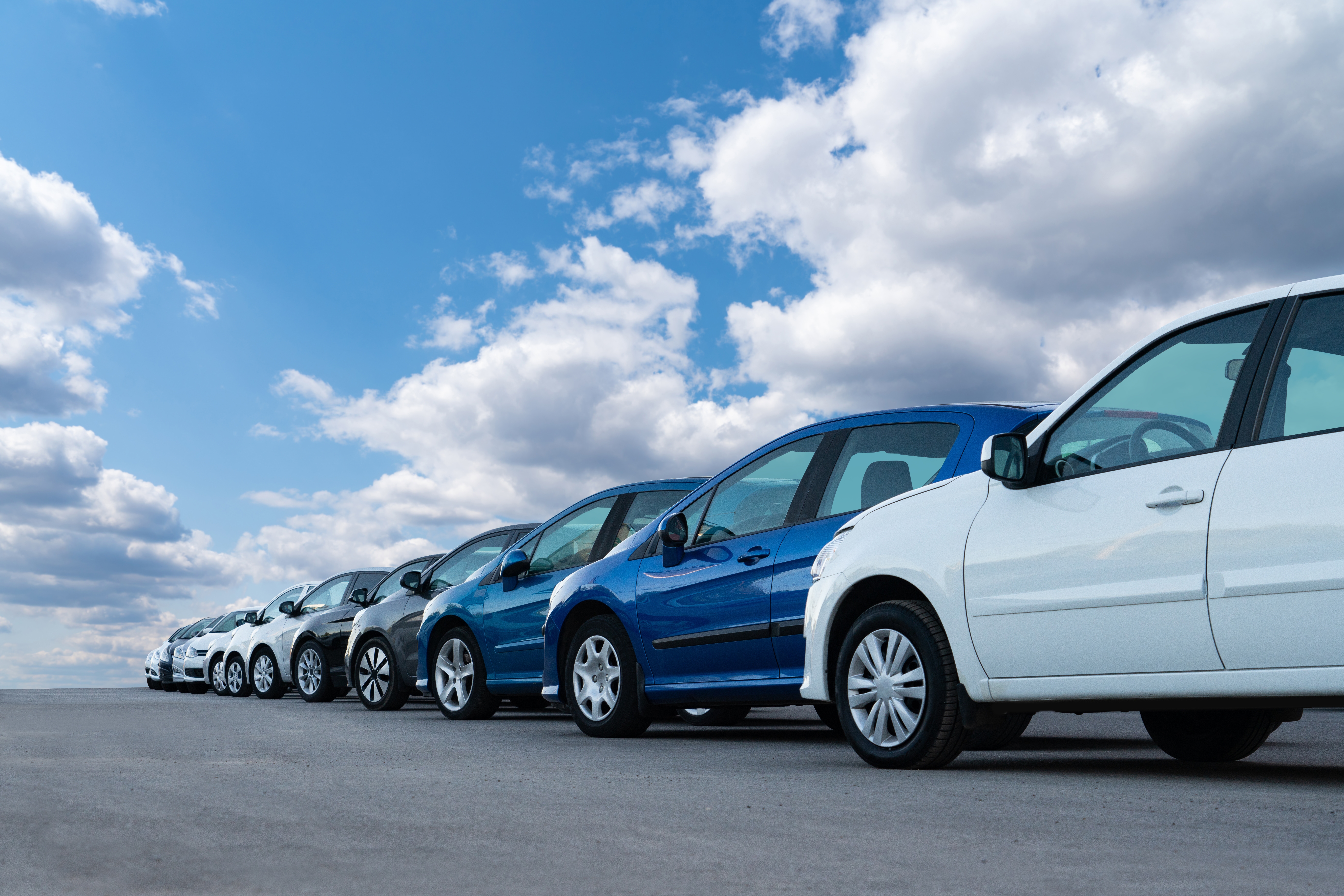 Row of parked cars lined up on a dealership lot under a blue sky