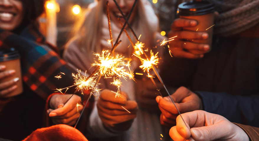 Hands holding lit sparklers at a nighttime celebration