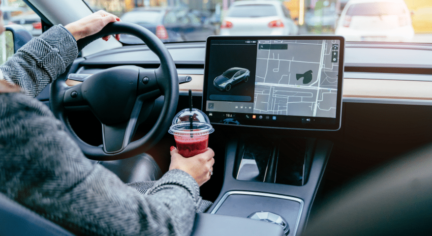 Driver holding a coffee beside a touchscreen in a Tesla