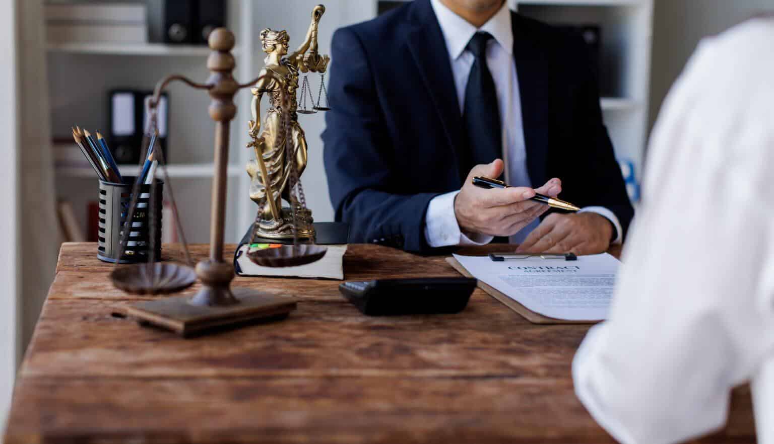 Scales of justice on a desk while an attorney consults with a client in the background