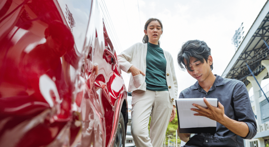 Red car with door damage as two people inspect it with a tablet