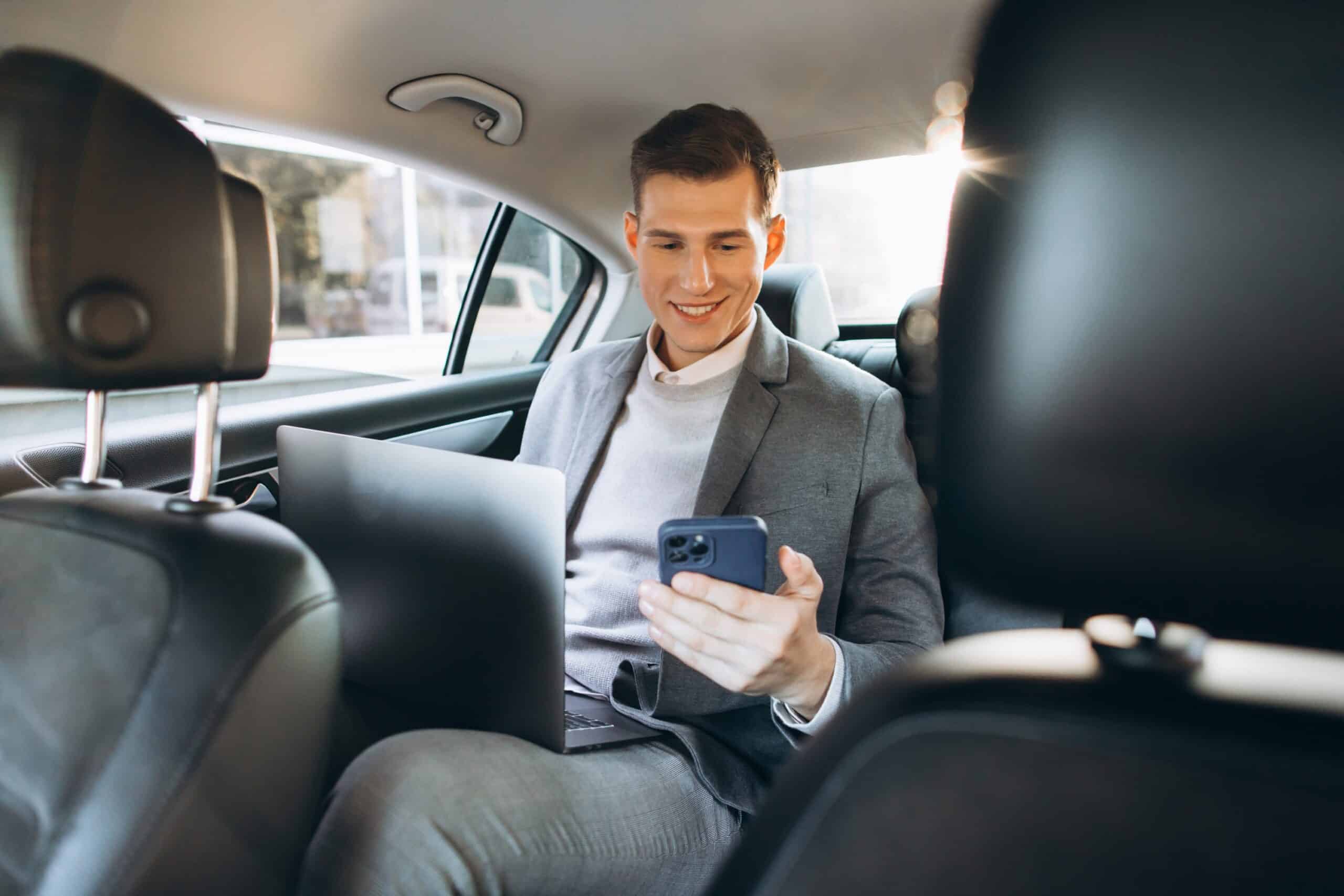 Man in a suit using his phone in the back seat of a car as a rideshare passenger