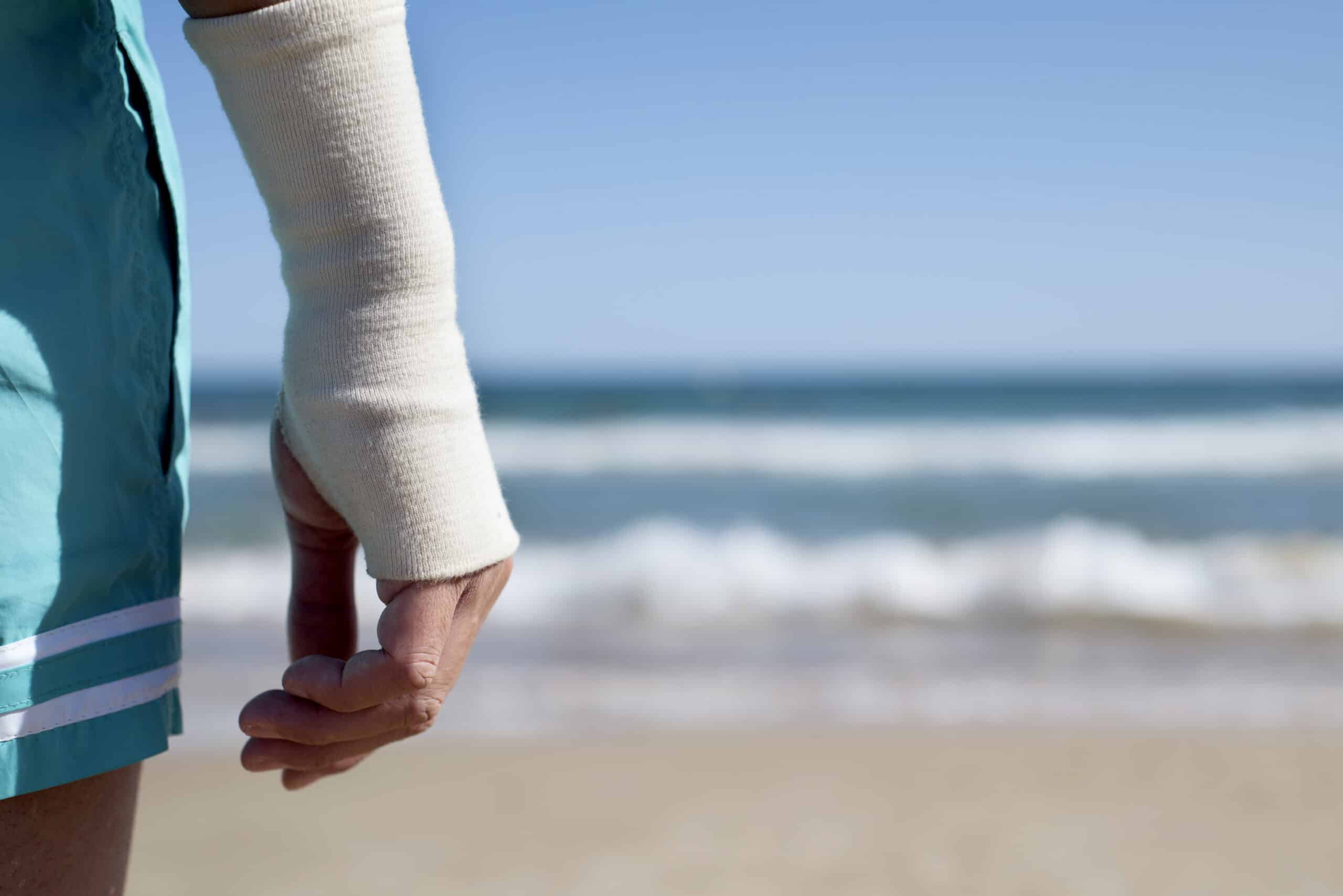 Person's bandaged arm raised with the ocean in the background