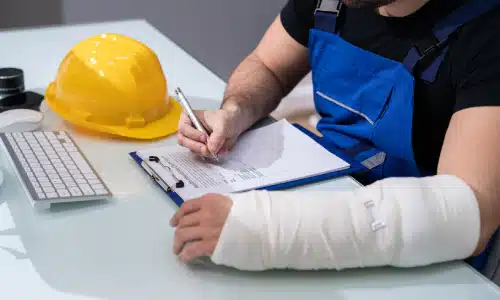 An injured hardhat worker filling out an insurance claim and resting his arm on the table.