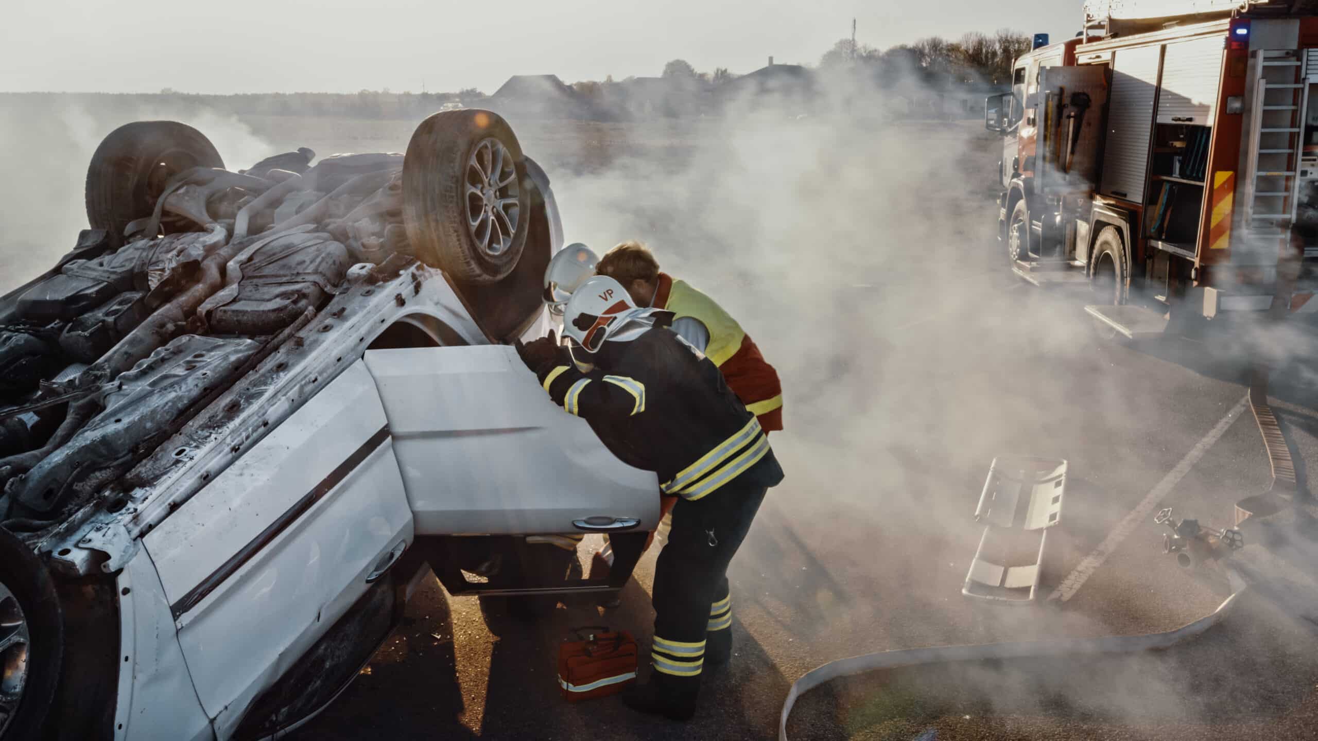 Overturned car resting on its roof with firefighters responding at the scene