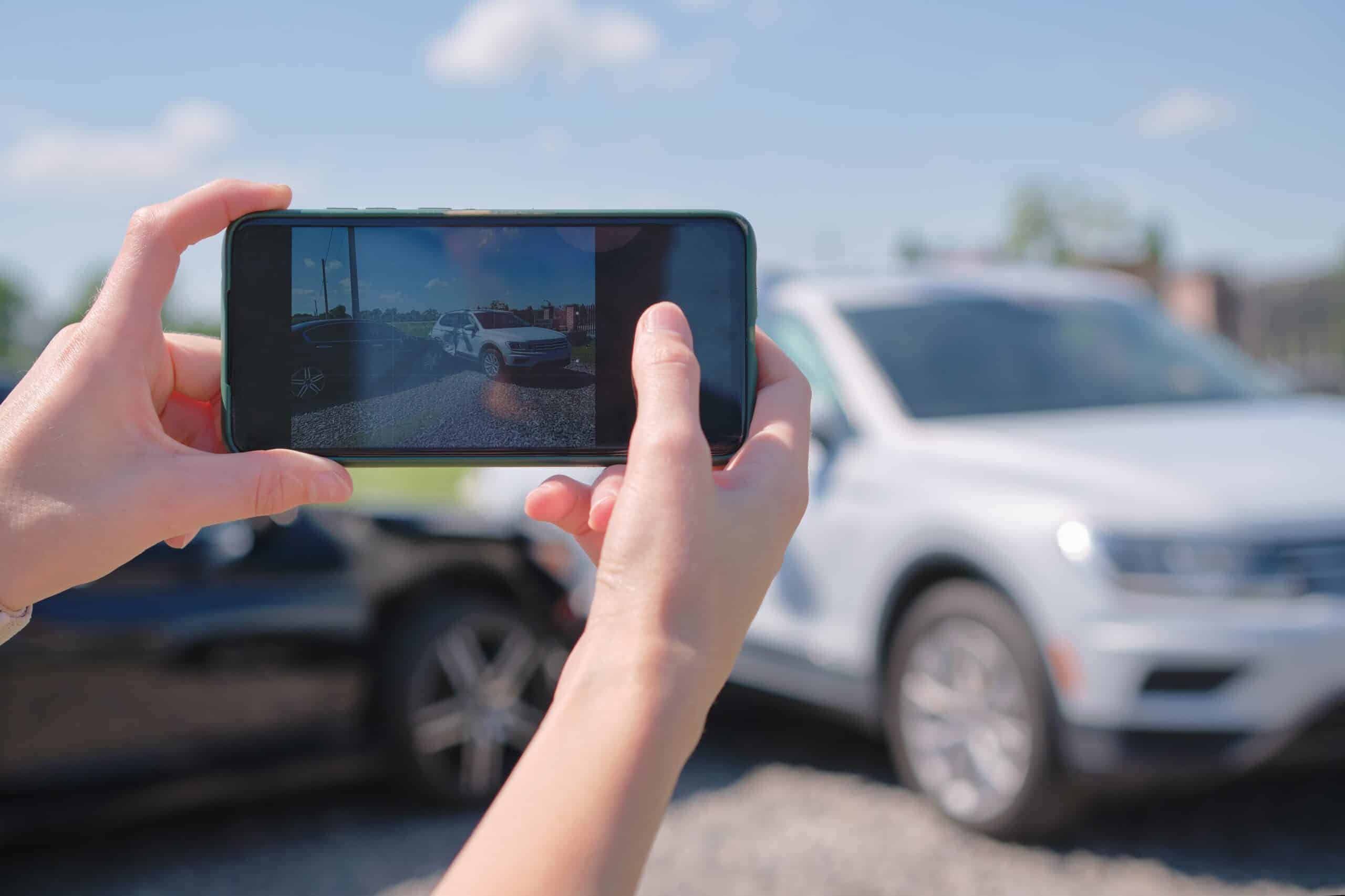 Hands photographing a damaged car with a smartphone to document an accident