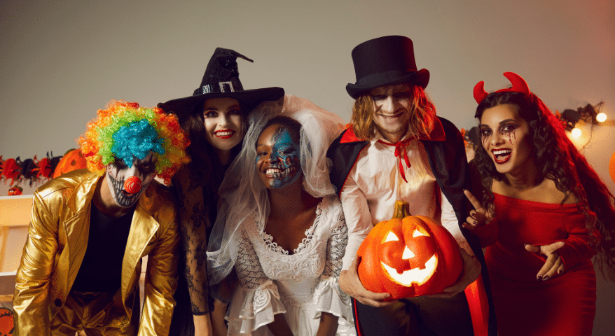 Group of people in Halloween costumes holding a jack-o-lantern