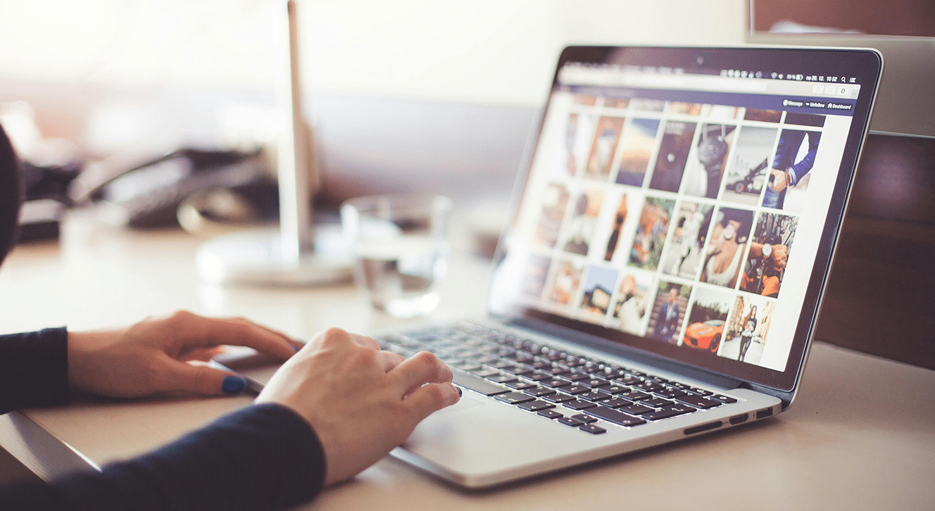 Close-up of hands using a laptop to view a photo gallery grid on a social media site.