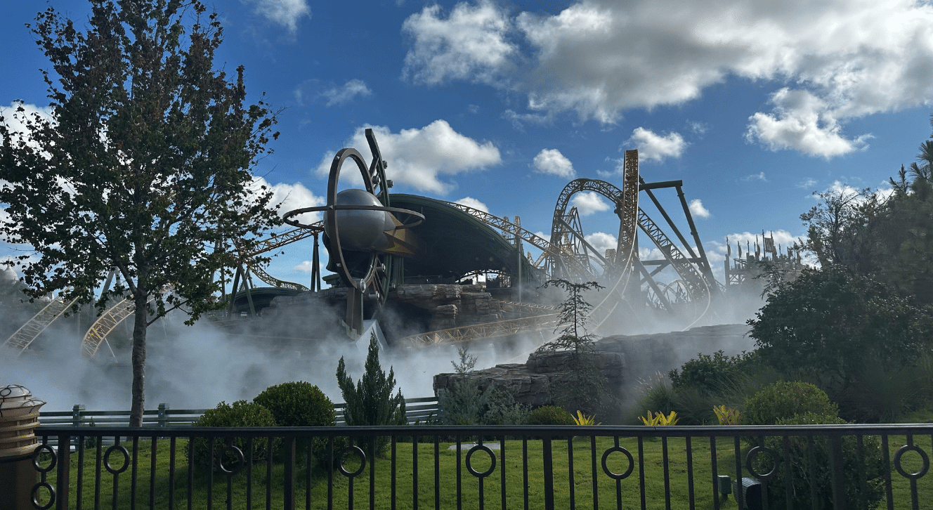 Large outdoor roller coaster with loops and steam effects under a blue sky.