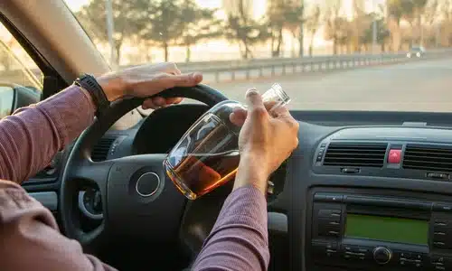 An over-the-shoulder shot of a driver drinking and driving on a public road.