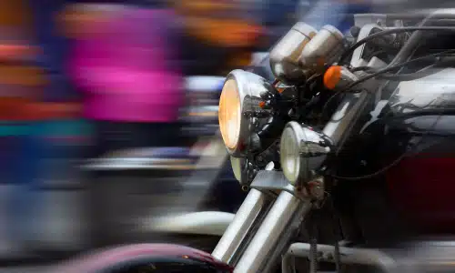 A motion-blurred shot of a big motorcycle driving past a crowd of people standing in the background.