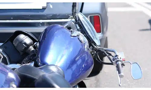 A lare blue motorcycle tilted to its side after colliding with the rear end of a grey car.