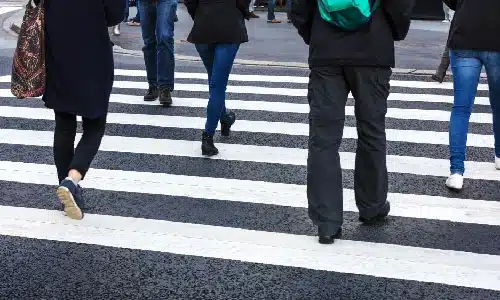 A small crowd of pedestrians crossing a busy road to get to work.