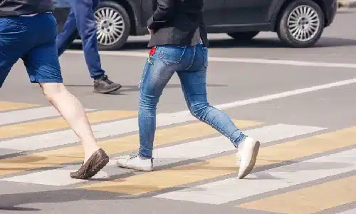 Pedestrians briskly walking along a crosswalk while a car in the background waits.