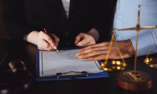 A personal injury lawyer assisting a client with filling up documents for a claim at his desk.