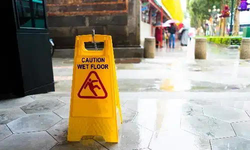 A yellow wet floor sign in front of a food business warning of danger caused by rain puddles.