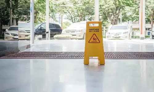 A yellow wet floor sign in front of a glass panel door warning of a hazard.