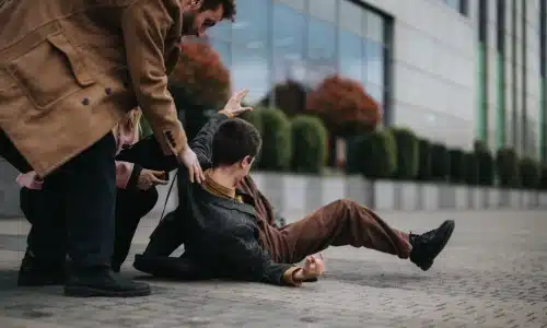 Two passersby helping up a person who fell down on a slippery walkway in front of a building.