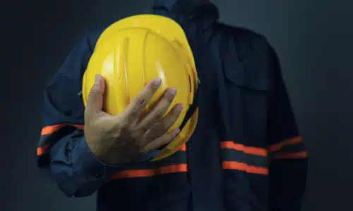 A chest-level shot of a hardhat worker holding his yellow helmet in front of his torso.