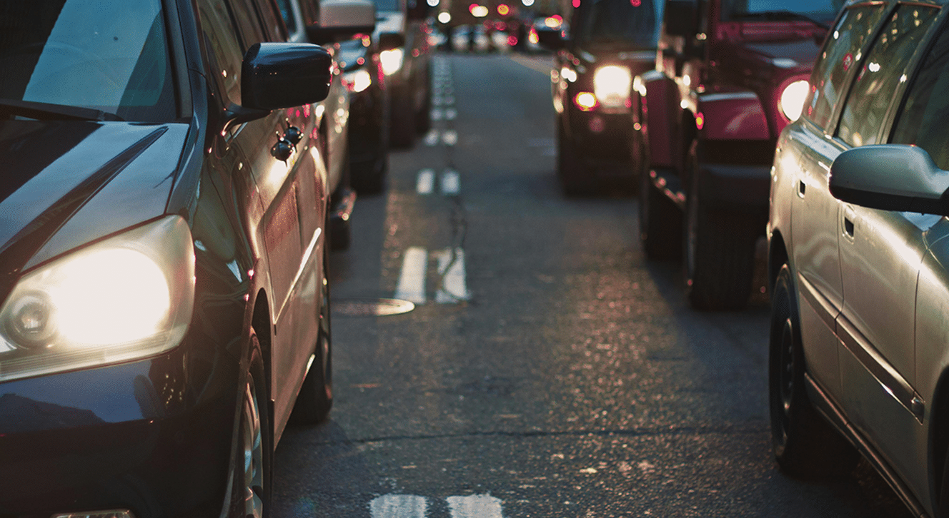Line of cars in heavy traffic with headlights on during the evening.