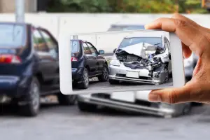 A smartphone capturing the aftermath of a severe car accident, showing the front of a badly damaged silver sedan.
