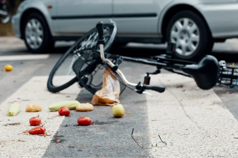 A busy street showing signs of a recent bicycle accident, with scattered debris and emergency responders in the background.