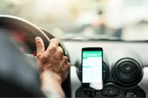 Driver’s hand on the steering wheel with a phone-mounted GPS, illustrating the risk factors involved in an Uber accident.