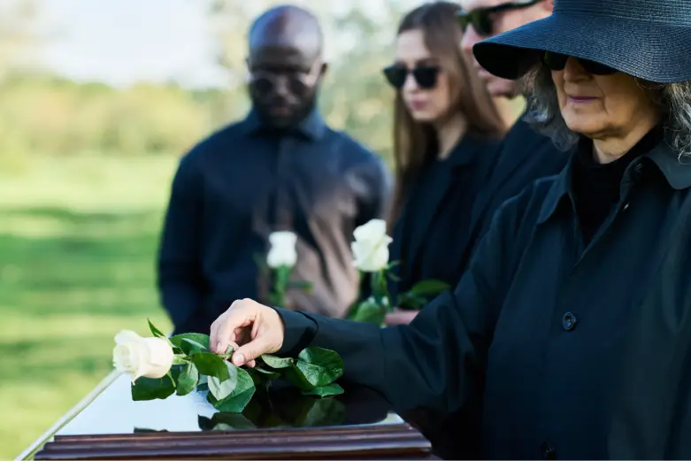 Group of individuals dressed in black placing white roses on a casket, reflecting the emotional impact of a wrongful death memorial service.