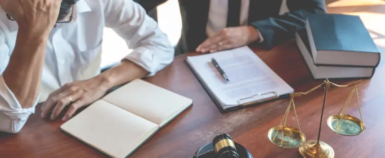 Distressed man consulting with a lawyer next to legal documents, scales of justice, and a gavel, symbolizing a wrongful death claim process.