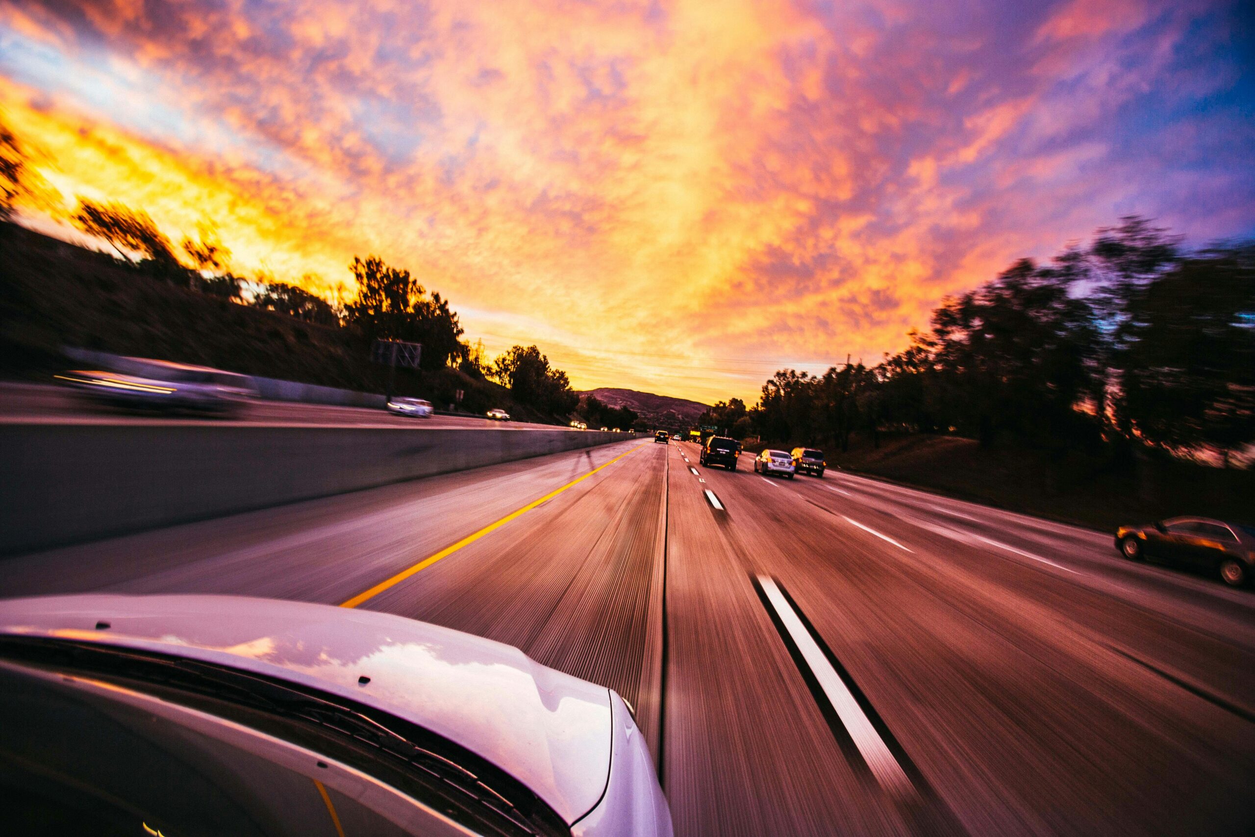 View from inside a car driving down a multi-lane highway during a colorful sunset