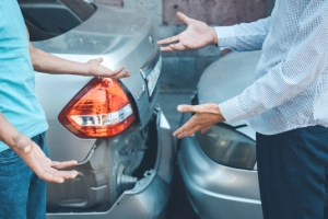 Two drivers arguing with each other at the scene of a car accident between their vehicles.