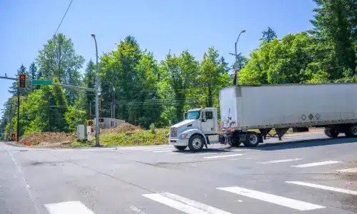 A semi-trailer truck running on the city crossroad intersection road with red traffic light.
