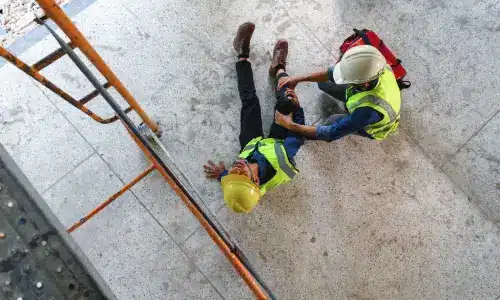 A first aid responder provides emergency care to a worker injured after falling from scaffolding onto the floor.