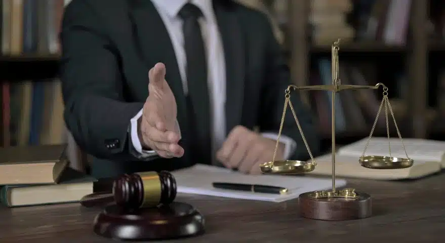 A slip and fall lawyer serving Florida holding a hand out for a handshake after signing a contract laid on an office desk