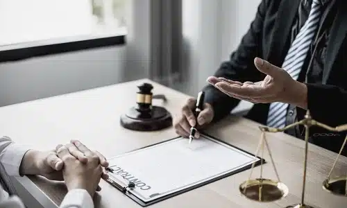 A catastrophic injury lawyer gestures with their left hand while talking to a client who is sitting on the opposite side of the office desk